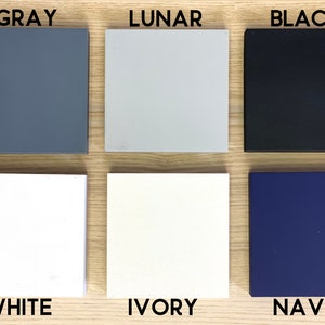 May include: Six paint color swatches on a wood surface. The colors are: Gray, Lunar, Black, White, Ivory, and Navy.