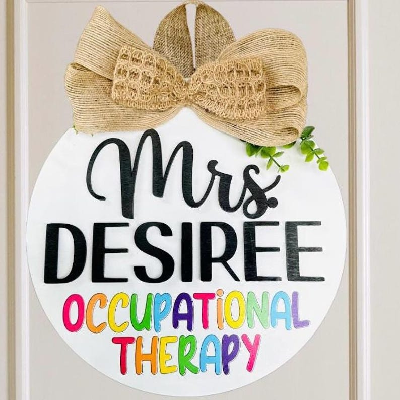 May include: A white round door hanger with a burlap bow. The text "Mrs. DESIREE OCCUPATIONAL THERAPY" is written in black and rainbow letters.