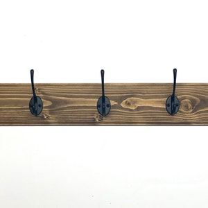 May include: A wooden coat rack with six black metal hooks. The rack is stained a dark brown color and has a rustic look.