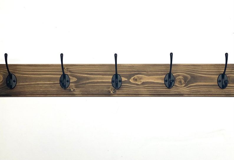May include: A wooden coat rack with six black metal hooks. The rack is stained a dark brown color and has a rustic look.