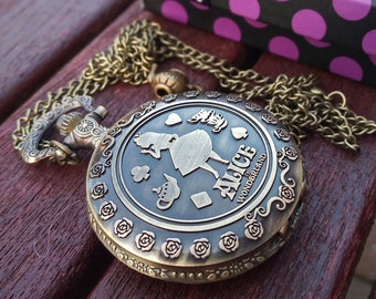 May include: A gold pocket watch with a chain and a design of Alice in Wonderland on the face. The watch is on a wooden surface with a purple and white polka dot gift box.