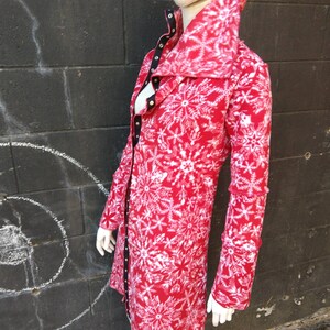 May include: A red long-sleeved jacket with a white snowflake pattern. The jacket has a high collar and a button closure.