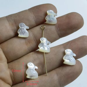 Puede incluir: Cinco abalorios de conejito de madreperla blanca con un aro de salto dorado. Los abalorios miden aproximadamente 3 cm de alto y 2 cm de ancho.
