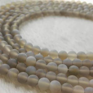 May include: A strand of grey matte round beads, with a smooth, frosted finish. The beads are arranged in a circular pattern, creating a necklace or bracelet.