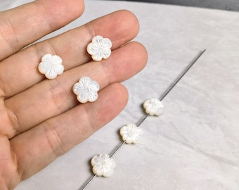Könnte beinhalten: Sechs weiße Perlmutt-Blumenperlen. Die Perlen sind auf einem silbernen Draht aufgefädelt.