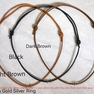 Puede incluir: Tres collares de cordón ajustables en marrón claro, negro y marrón oscuro. Cada cordón presenta dos nudos deslizantes y una pequeña argolla metálica en la parte inferior. Etiquetas de texto identifican los colores y argollas sueltas.