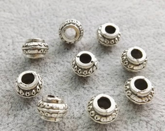 May include: Eight round silver-toned metal beads featuring a raised, textured pattern around the center and a smooth, circular opening at the top. Each bead has a slightly weathered finish with dark recessed areas highlighting the intricate details.