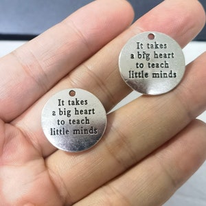Puede incluir: Dos colgantes de plata con el texto "Se necesita un gran coraz&oacute;n para ense&ntilde;ar a las mentes peque&ntilde;as" en cada uno.