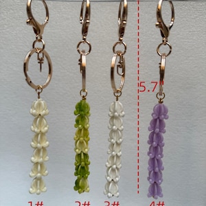 May include: Four keychains with gold-tone lobster clasps and rings, each featuring a dangling floral-shaped charm in cream, green, white, or purple. A red dashed line indicates a total length of 5.7 inches, with labels 1#, 2#, 3#, and 4# below.