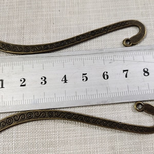 Puede incluir: Dos marcapáginas de bronce antiguo con un diseño decorativo de espiral. Los marcapáginas miden aproximadamente 7 cm de largo y tienen un gancho en la parte superior.