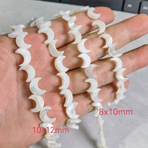 Op de afbeelding: Meerdere strengen witte, halvemaanvormige kralen. De kralen zijn parelmoerachtig en aan elkaar geregen. De kralen zijn 8x10mm en 10x12mm groot. Deze kralen zijn waarschijnlijk bedoeld voor het maken van sieraden.