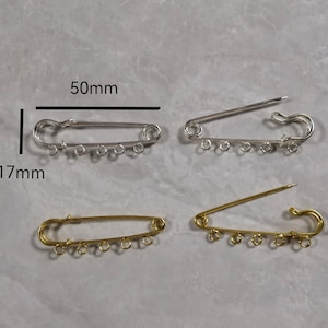 May include: Two safety pins with five jump rings each. The safety pin on the left is gold and measures 1.97 inches long. The safety pin on the right is silver and measures 1.97 inches long.