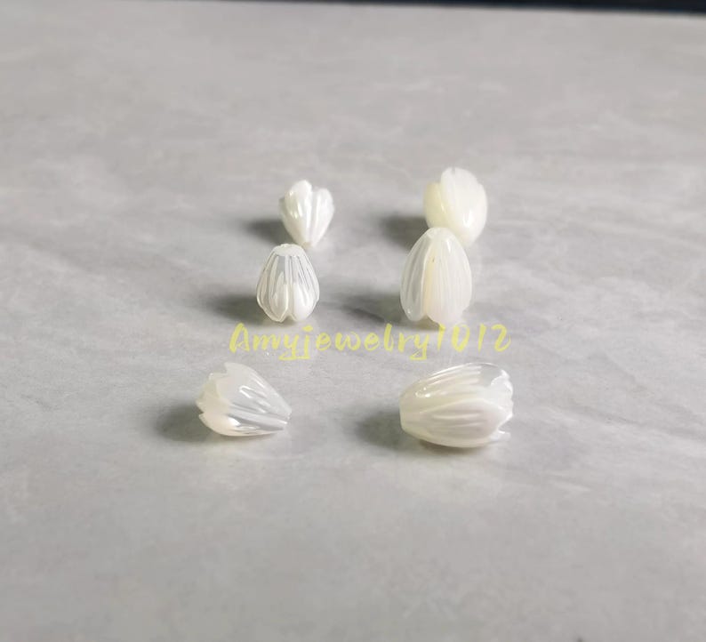 May include: Six white, iridescent, flower-shaped beads arranged in two columns. Each bead features carved petal details with a smooth, glossy finish. The text "Amyjewelry1012" is printed in yellow across the center of the image between the beads.