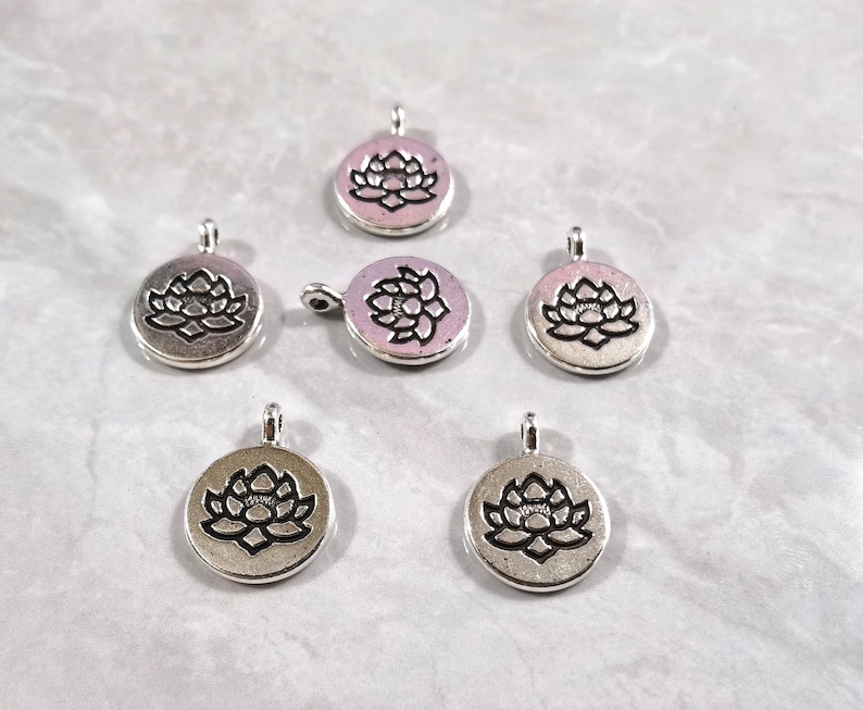 May include: Six silver-toned metal charms with a lotus flower design. The charms are round and have a loop at the top for attaching to jewelry or other crafts.