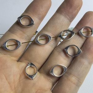 以下が含まれることがあります： 手の中に、テクスチャ加工された表面を持つ銀製の目の形をしたリングが8つあります。リングは細い金の紐でつながっています。