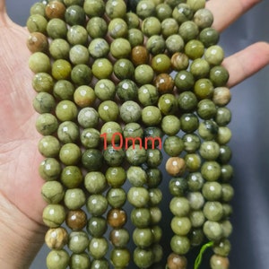 May include: A strand of green and brown gemstone beads, each bead is approximately 10mm in diameter. The beads have a faceted, slightly irregular shape.