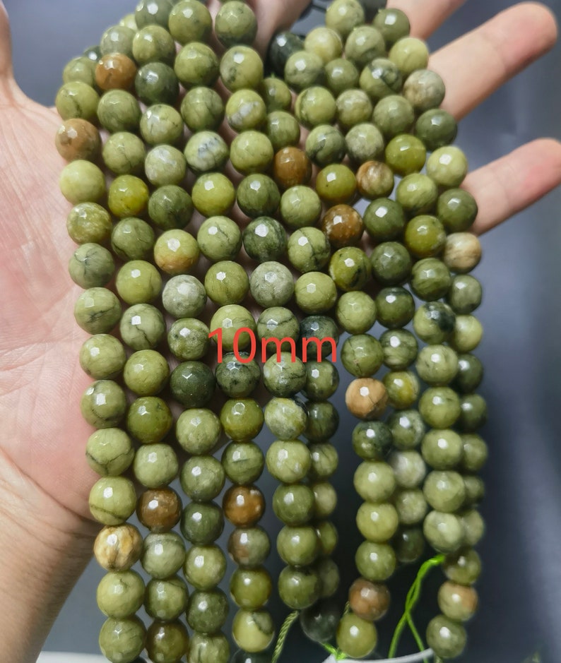 May include: A strand of green and brown gemstone beads, each bead is approximately 10mm in diameter. The beads have a faceted, slightly irregular shape.