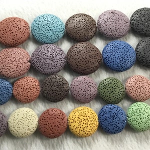 Puede incluir: Una colección de cuentas redondas de roca volcánica en varios colores, incluyendo marrón, gris, azul, verde y amarillo. Las cuentas son todas aproximadamente del mismo tamaño y tienen una superficie rugosa y texturizada.