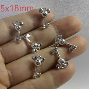 Könnte beinhalten: Fünf silberfarbene Metallanhänger in Form von Schlüsseln mit abgerundeten, mausohrähnlichen Oberteilen und herzförmigen Unterteilen. Jeder Anhänger misst 10,5x18mm. Die Schlüsselanhänger haben eine glatte, reflektierende Oberfläche.