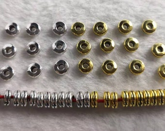 May include: A collection of small, round, metallic beads with a central hole. The set includes silver-toned and gold-toned beads arranged in three rows of loose pieces, with a single red string threaded through a row of matching beads.
