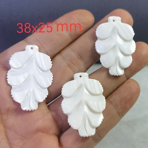 Peut inclure: Trois pendentifs en forme de feuille en coquille blanche avec un motif sculpté. Chaque pendentif mesure 38 x 25 mm.