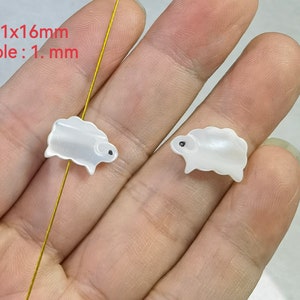 May include: Two white shell sheep beads with black eyes. The beads are 11x16mm with a 1mm hole.