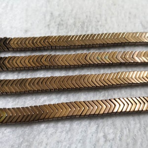 May include: Four strands of gold chevron-shaped beads. The beads are arranged in a zig-zag pattern.