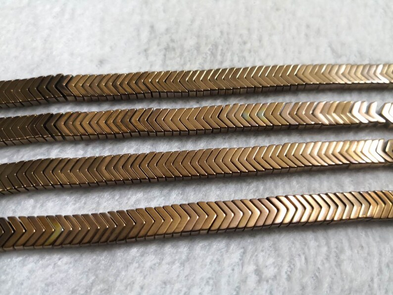 May include: Four strands of gold chevron-shaped beads. The beads are arranged in a zig-zag pattern.