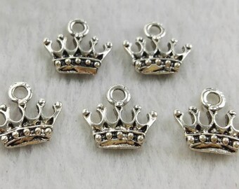 Puede incluir: Cinco dijes de corona de metal en tono plateado, cada uno con un pequeño lazo circular en la parte superior para su fijación. Los dijes tienen un acabado detallado y envejecido con detalles de cuentas en relieve en la base y cinco puntas.