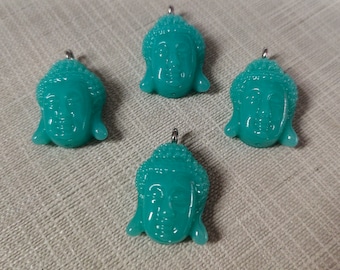 May include: Four teal blue glass Buddha head charms with silver jump rings. The charms are detailed with a textured surface and a serene facial expression.