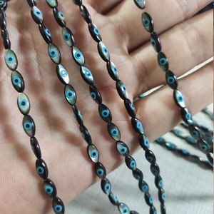 May include: A strand of black and blue oval-shaped beads with an evil eye design. The beads are strung on a clear thread.