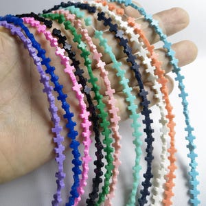 Puede incluir: Una hebra de cuentas con forma de cruz en varios colores, incluyendo rosa, azul, verde, blanco y naranja. Las cuentas están enhebradas en un hilo transparente y tienen aproximadamente 1,25 cm de tamaño.