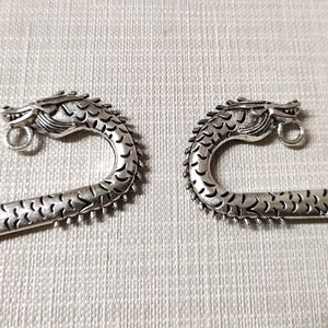 May include: Two silver-toned metal bookmarks, each featuring a detailed dragon head at the curved top. The dragon design includes textured scales along the neck and body, with a small circular loop attached beneath the chin for hanging charms.