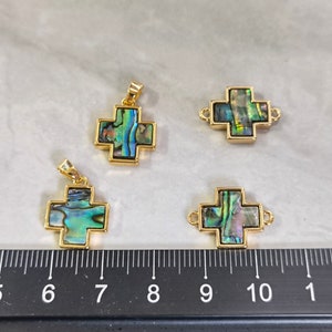 Op de afbeelding: Vier gouden kruisbedels met inleg van abalone-schelp. De kruisen zijn ongeveer 2,5 cm groot en hebben een lus aan de bovenkant om aan een ketting of koord te bevestigen.