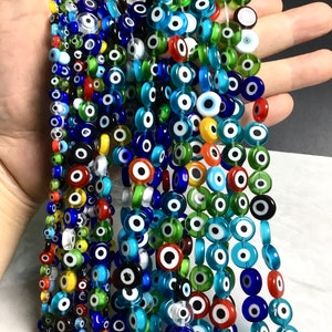Könnte beinhalten: Eine Strähne bunter Glasperlen mit einem bösen Augen-Design. Die Perlen sind rund und haben eine weiße Mitte mit einer schwarzen Pupille. Die Perlen sind auf einem durchsichtigen Faden aufgefädelt und in verschiedenen Farben erhältlich, darunter Blau, Grün, Rot und Gelb.