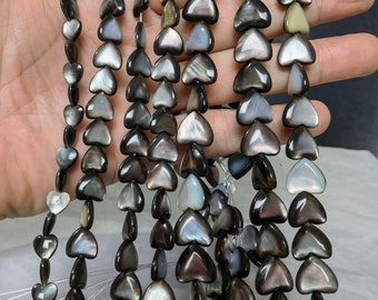 May include: A strand of black and iridescent heart-shaped beads. The beads are made of mother of pearl and have a smooth, polished finish.