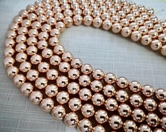 Op de afbeelding: Een streng rose gouden kralen, elke kraal is rond en glad. De kralen zijn in een cirkelvormige patroon gerangschikt, waardoor een mooie en elegante uitstraling ontstaat.