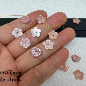 Op de afbeelding: Kleine, lichtroze, vijfbladige bloemvormige kralen met een iriserende afwerking. Elke kraal heeft een diameter van 12 mm met een centraal gat van 1 mm. De kralen hebben een uitgesneden, radiale bloembladtextuur en een glad, glanzend oppervlak.