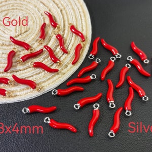 Könnte beinhalten: Eine Sammlung roter Chili-Anhänger mit goldenen und silbernen Akzenten. Die Anhänger sind 18 mm x 4 mm groß und auf einer gewebten Oberfläche und einem schwarzen Hintergrund angeordnet. Die Wörter "Gold" und "Silber" sind auf der Oberfläche geschrieben.