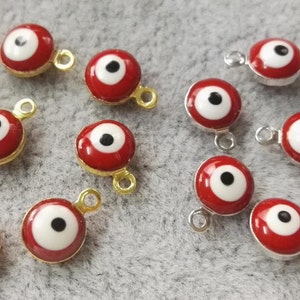 Könnte beinhalten: Eine Sammlung von roten und weißen bösen Augen-Anhängern mit goldenen und silbernen Sprungringen. Die Anhänger sind rund und haben eine weiße Mitte mit einer schwarzen Pupille. Die Anhänger sind perfekt, um Schmuck, Schlüsselanhängern oder anderen Bastelarbeiten einen Hauch von Schutz und Glück zu verleihen.