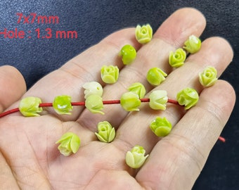 May include: A collection of 17 green and white carved flower beads with a 7mm x 7mm size and a 1.3mm hole. The beads are strung on a red elastic cord.