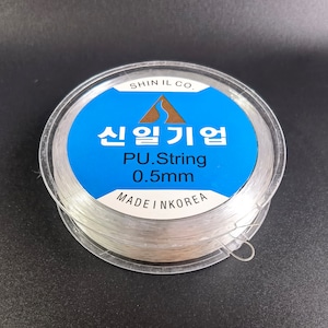 May include: A spool of clear 0.5mm PU string, made in Korea. The label reads "Shin Il Co. 신일기업 PU.String 0.5mm MADE IN KOREA".