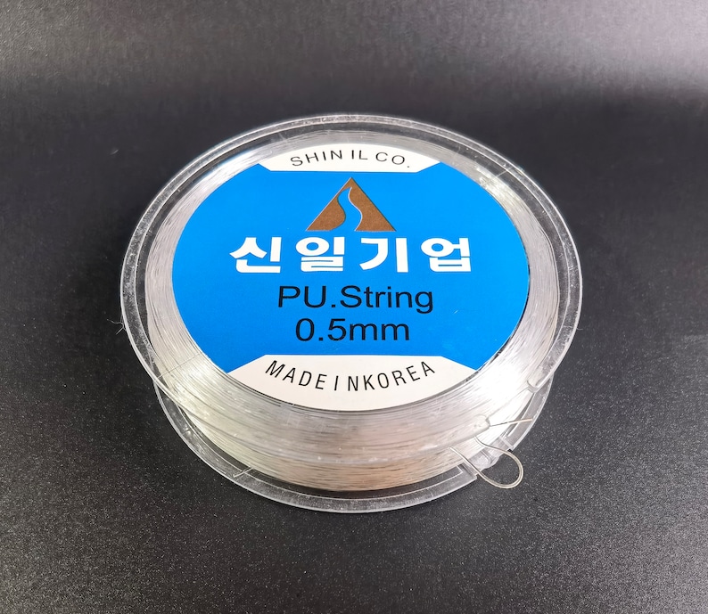 May include: A spool of clear 0.5mm PU string, made in Korea. The label reads "Shin Il Co. 신일기업 PU.String 0.5mm MADE IN KOREA".