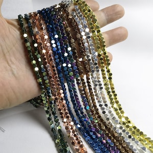 Può includere: Assortimento di perline esagonali sfaccettate da 4 mm in vari colori metallici, tra cui oro, argento, oro rosa, blu, verde e viola. Le perline sono infilate su uno sfondo bianco.