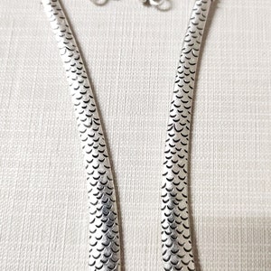May include: Two silver-toned metal bookmarks, each featuring a curved top shaped like a dragon head with detailed scales along the length of the body. The dragon heads are oriented toward each other, and each includes a small circular loop at the chin.