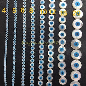 May include: Eight vertical strands of round white beads with blue and black circular centers, arranged by size from left to right. The strands are labeled with yellow numbers 4, 5, 6, 8, 10, 12, 15, and 20, indicating the bead diameter in millimeters.