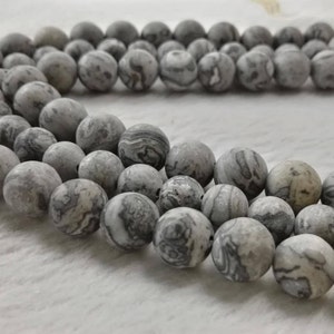 May include: A strand of gray and white marbled round beads. The beads are smooth and have a natural, organic look.