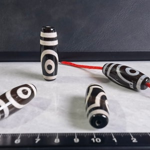 May include: Four black and white agate beads with a red string. The beads have a circular pattern with a white center and black rings around it.
