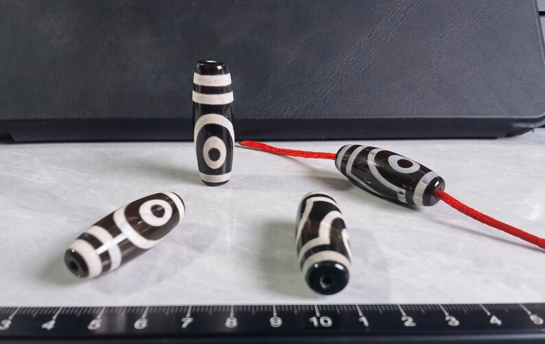 May include: Four black and white agate beads with a red string. The beads have a circular pattern with a white center and black rings around it.