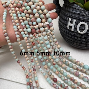 May include: Strands of round gemstone beads in varying sizes, including 6mm, 8mm, and 10mm. The beads feature a mix of colors, including light blue, beige, and reddish-brown, creating a natural, earthy aesthetic. Ideal for jewelry making.